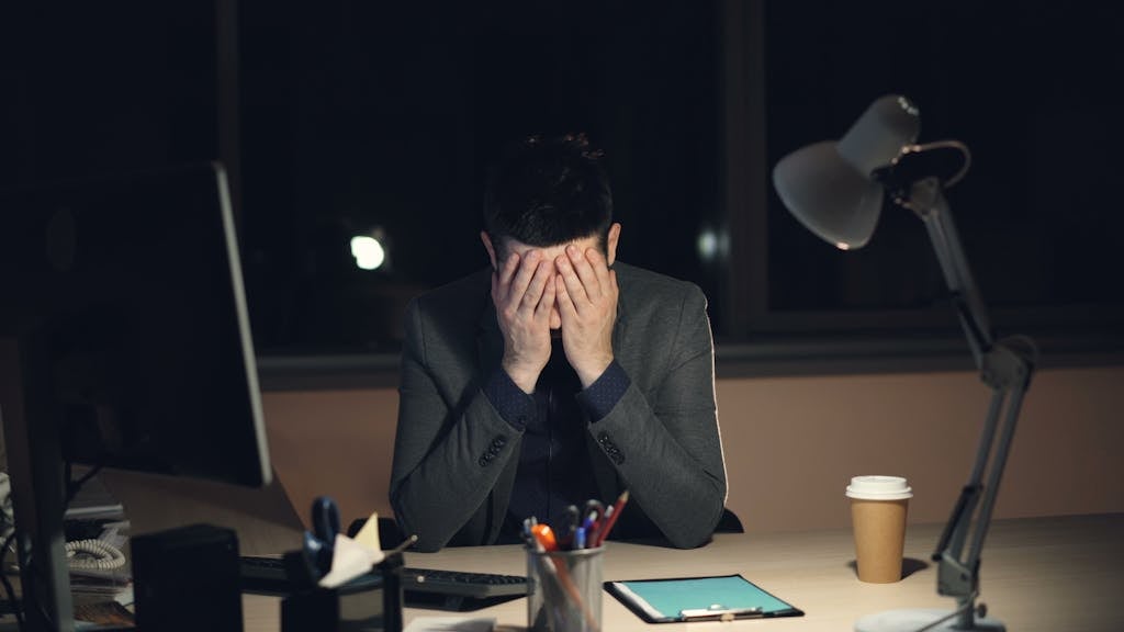 Why Financial Anxiety Feels Worse at Night Businessman overwhelmed and stressed at his desk during late-night work hours.
