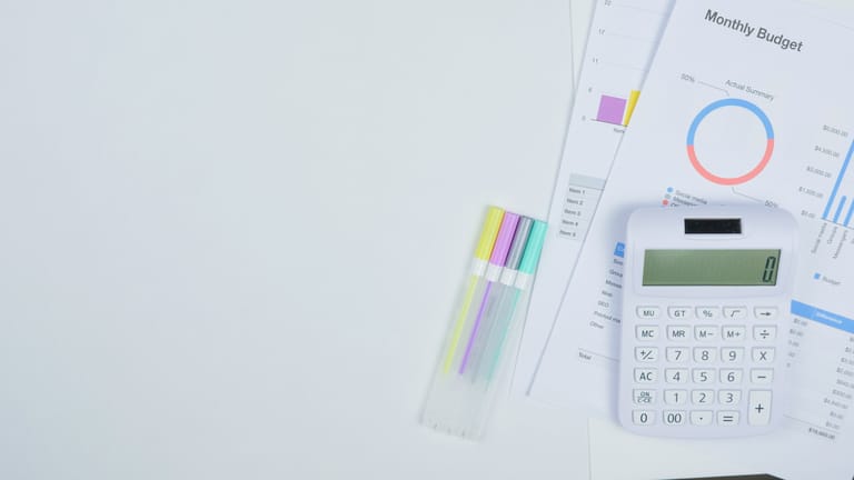 Minimalist office desk with a calculator, budget planning documents, and colorful pens.