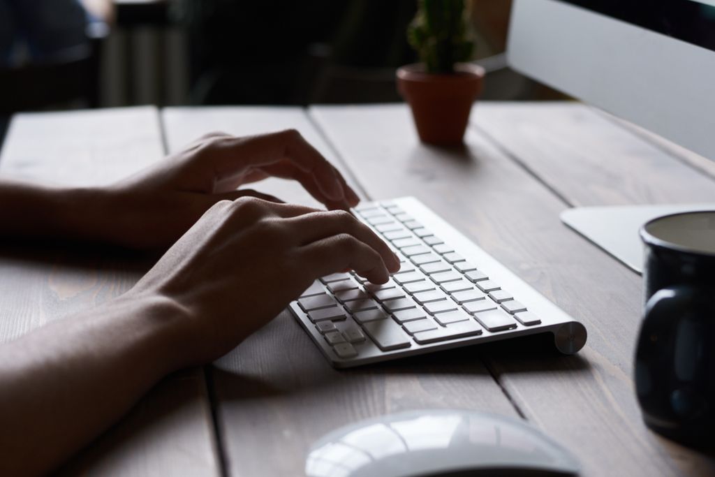 photo by fauxels Close-up of hands typing on a wireless keyboard at a modern workspace.