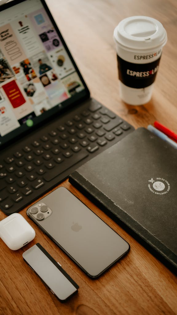 photo by yeŞ From above of tablet with tablet docking tablet placed on wooden table with cellphone near netbook and paper cup of takeaway coffee near wireless earbuds case